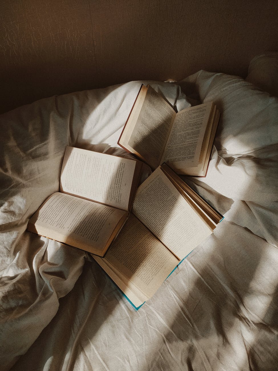 Opened books placed on disheveled bed.