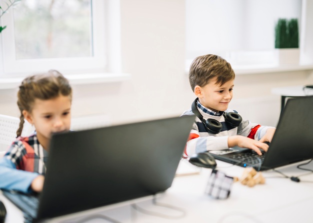 Smiling portrait of a boy using laptop sitting with a girl in the classroom