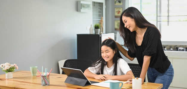 A young mother is teaching a daughter to do homework at the wooden table taking care of important aspects of her education